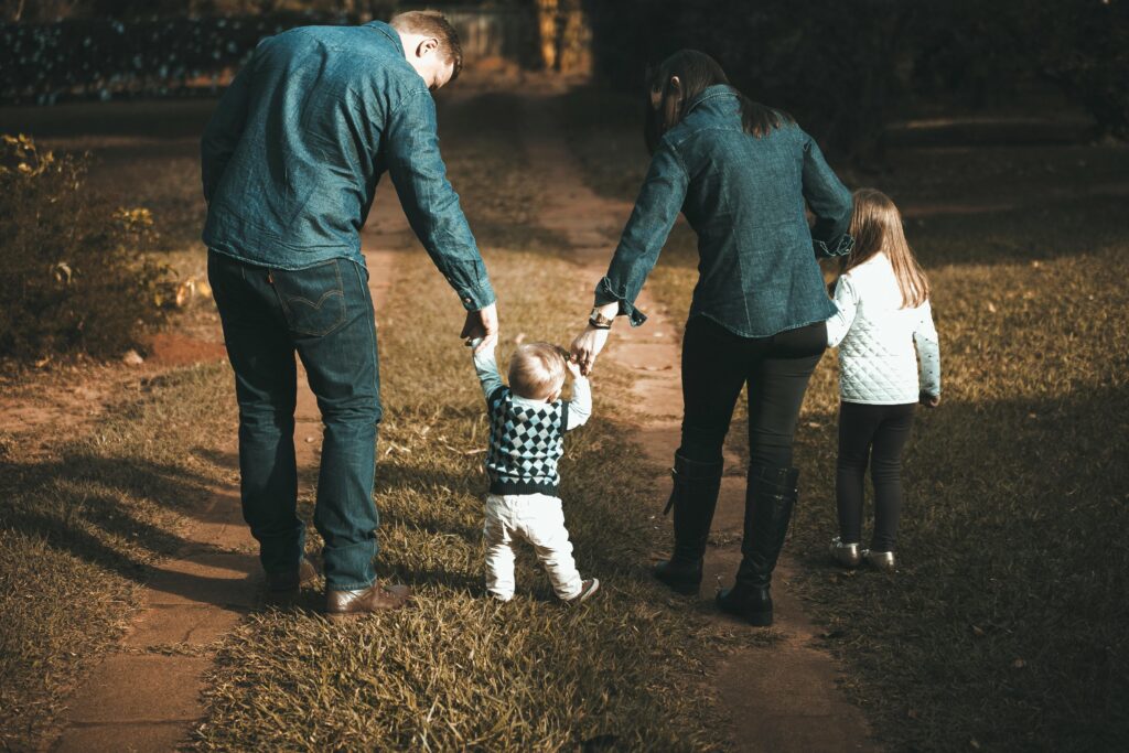 A family of four walks hand in hand on a path, enjoying a sunny day outdoors.